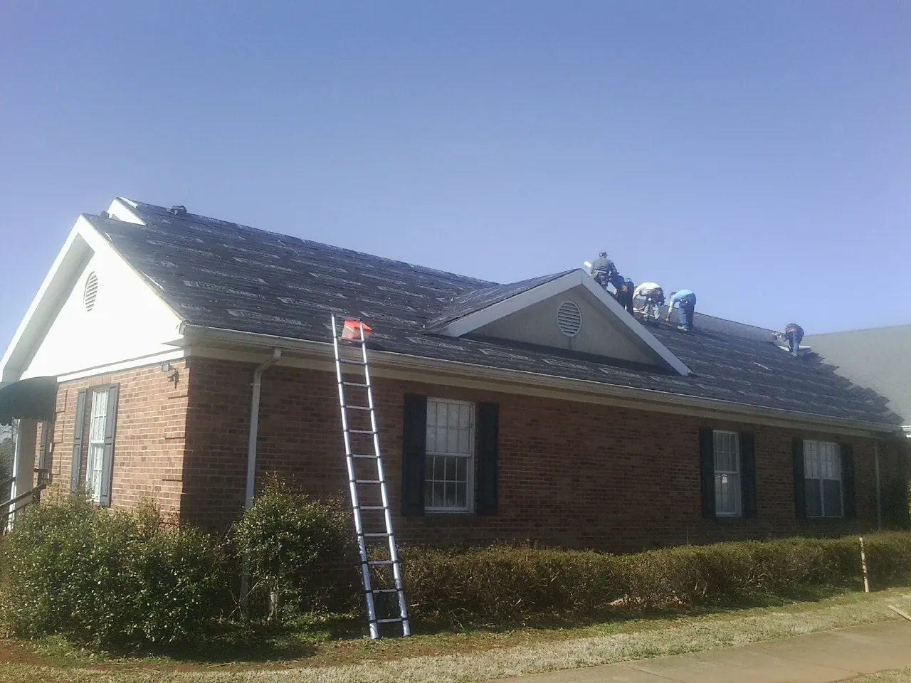 Crew tearing shingles off a brick ranch roof with a ladder set — Emergency Roof Repair work by our crew in Fishkill